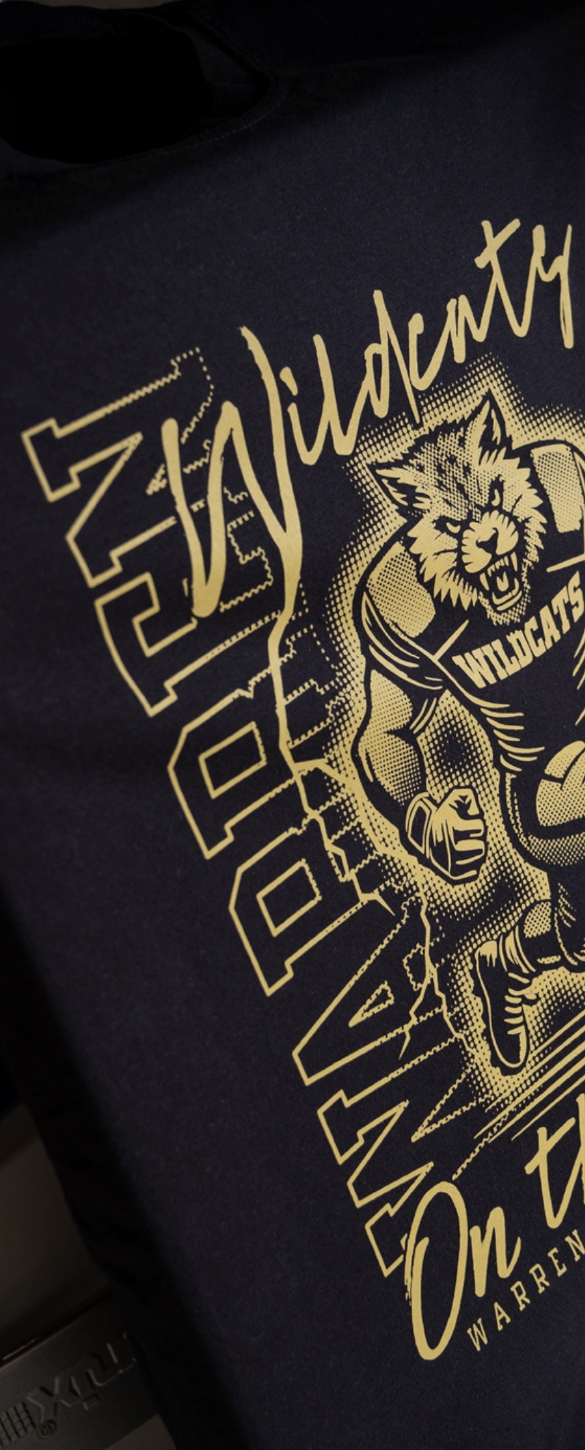 Black shirt with gold graphic design and text on a dark background
